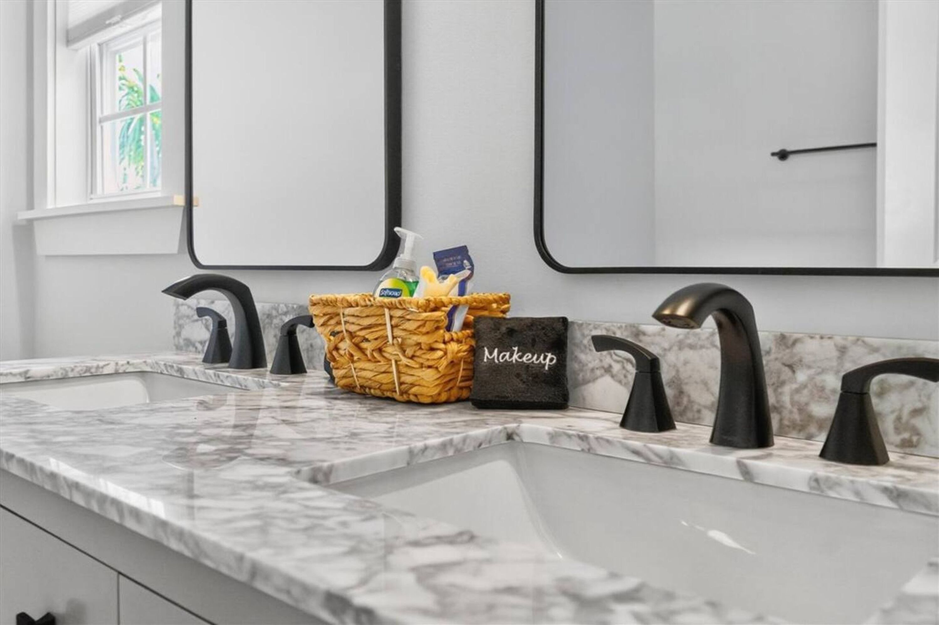 A bathroom with a marble countertop, three black faucets, and a wicker basket containing toiletries.