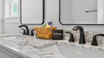 A bathroom with a marble countertop, three black faucets, and a wicker basket containing toiletries.