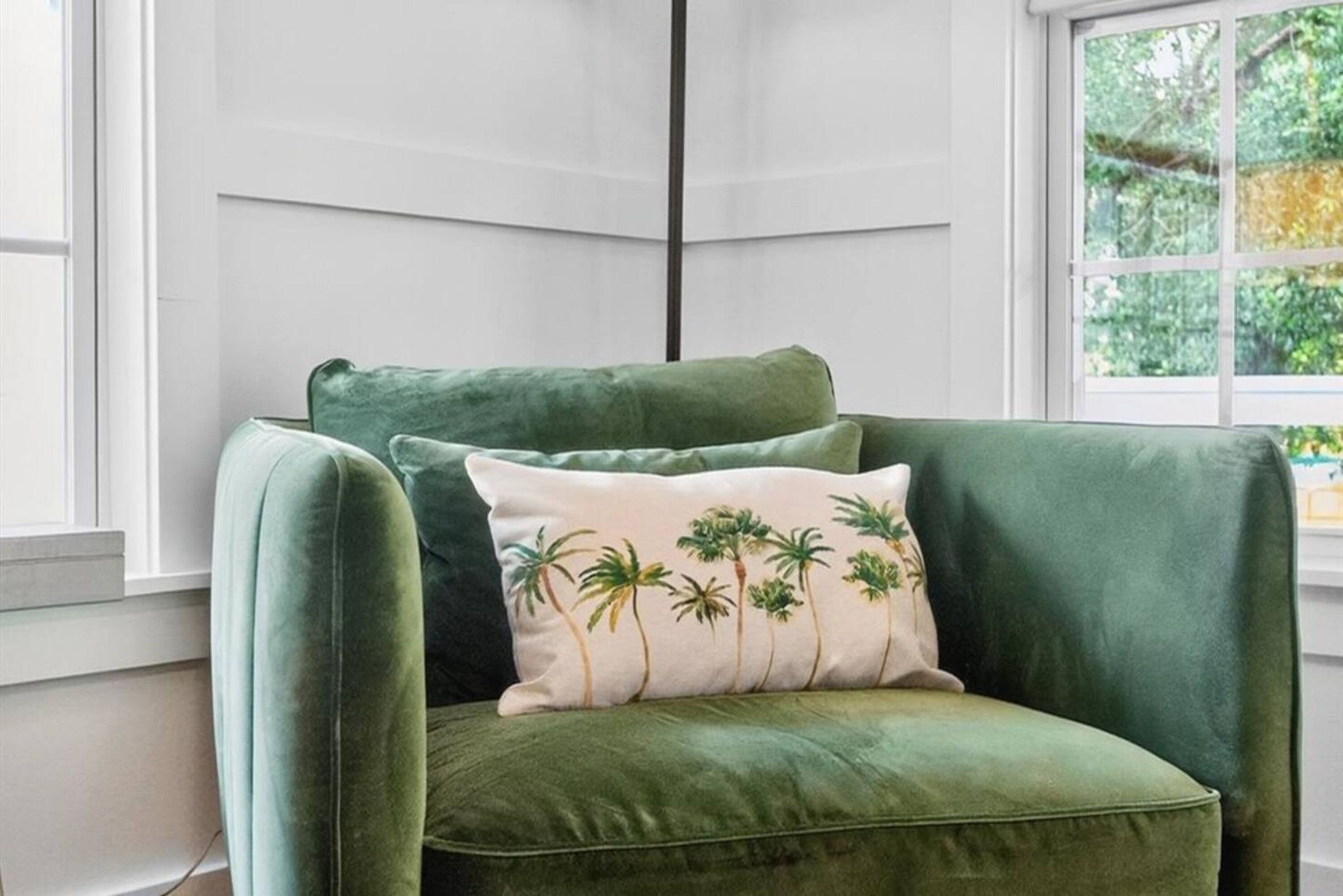 Un sillón verde de terciopelo con un cojín con estampado de palmera.