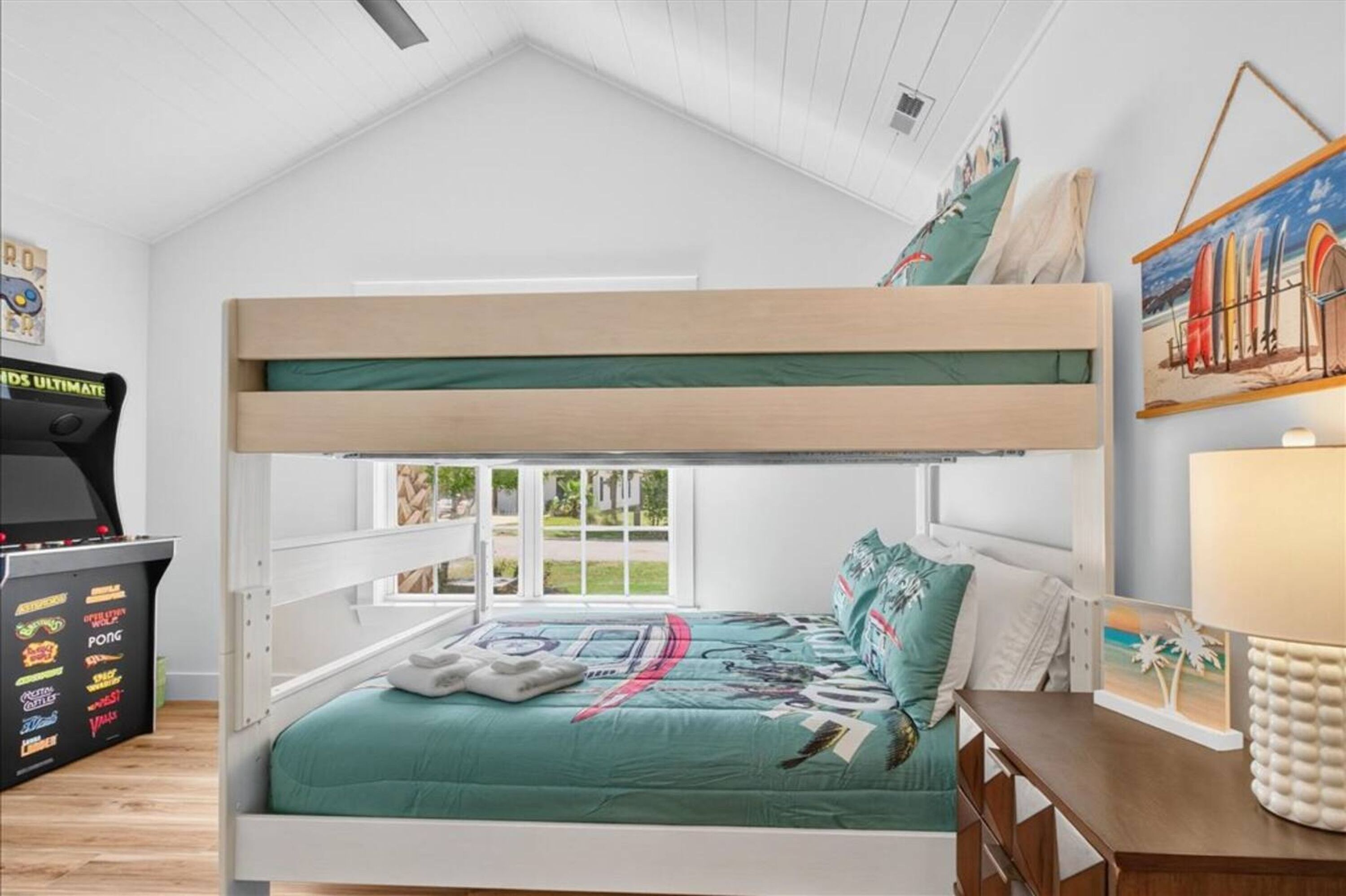 A bunk bed with a view of the outdoors, a desk with a lamp, and a wall with a painting.