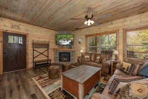 A cozy cabin interior with a fireplace, wooden furniture, and a large window overlooking a forest. - Lux Cabin Mtn Views Flat Parking Dog Friendly (Gatlinburg)