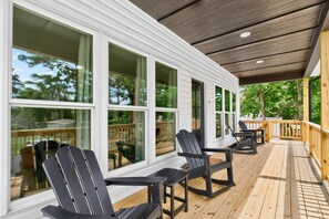 A covered outdoor deck with Adirondack chairs and a table, large windows, and a wooden railing. - New Listing Luxury House 5 Min Walk to Beach (Oak Island)
