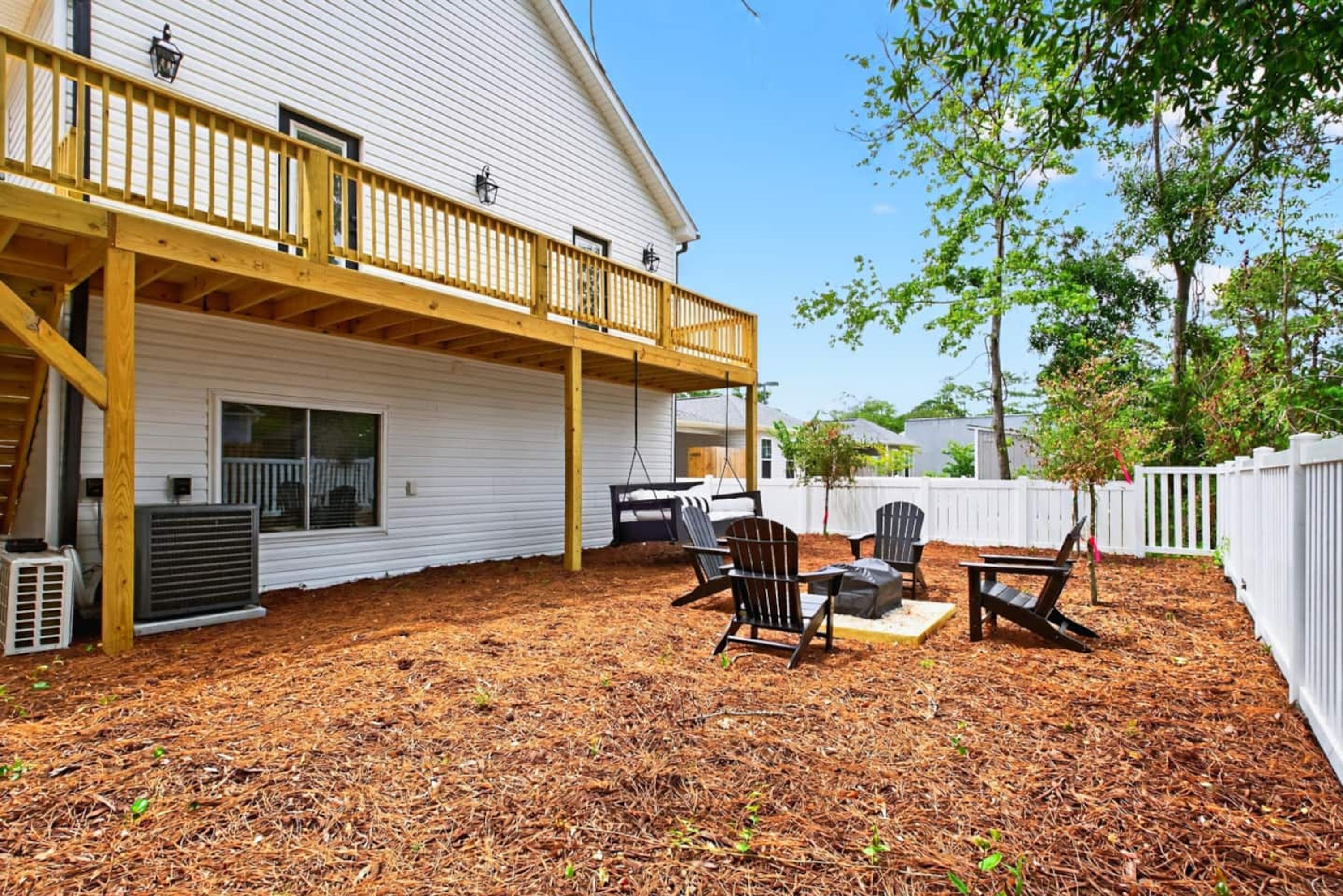 A covered patio with outdoor seating, a white building, and a white fence.