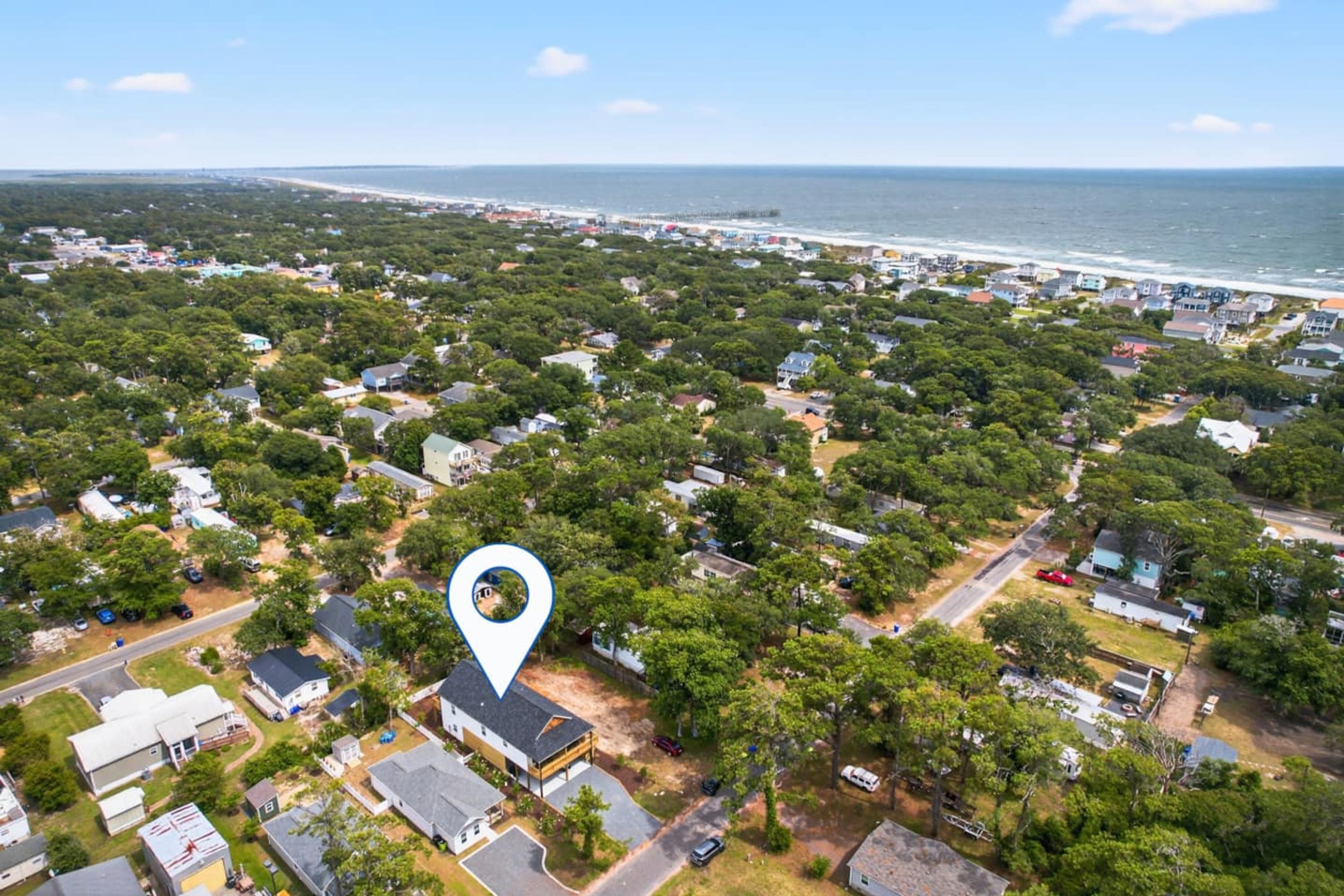 Luchtbeeld van een kustgebied met woonhuizen, zowel vrijstaande woningen als kleinere gebouwen, omgeven door weelderige begroeiing en een strand op de achtergrond.