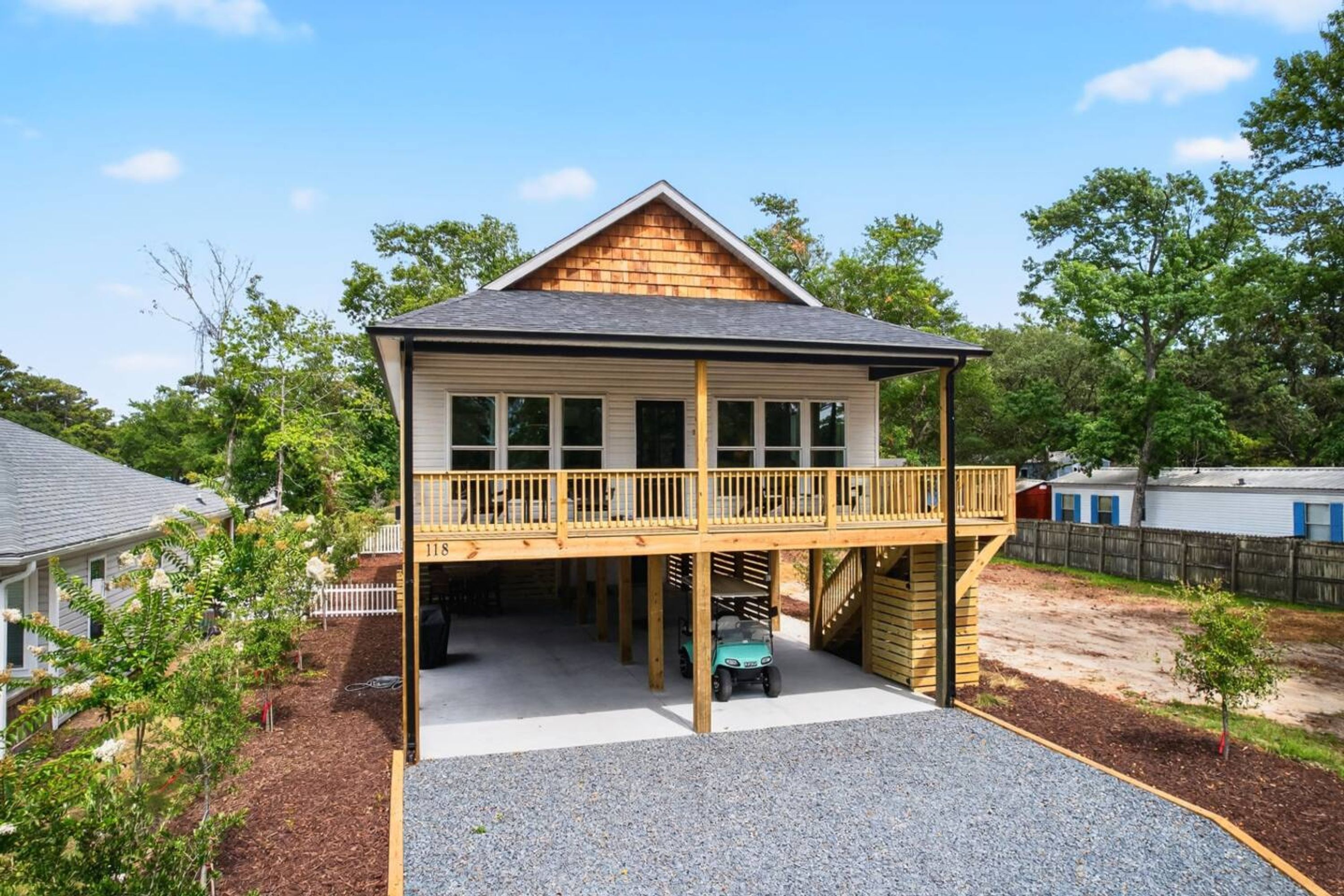 Een tweelaags huis met een balkon, een overdekte veranda en een klein voertuig dat eronder geparkeerd staat.
