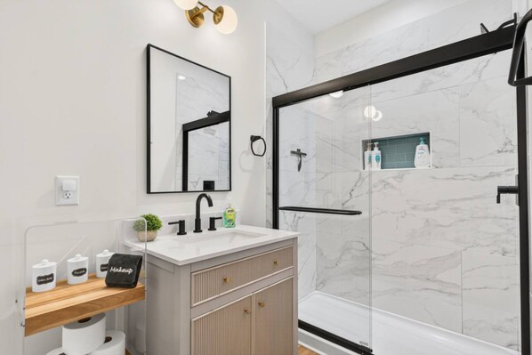 Une salle de bain moderne avec une douche en marbre, un grand miroir et un meuble-lavabo avec un évier et des rangements.