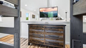 Uma sala de estar moderna com um suporte de televisão de madeira, uma TV de tela plana e uma parede branca com um quadro emoldurado.