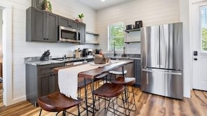 Uma cozinha moderna com armários escuros, eletrodomésticos de aço inoxidável, bancada de mármore e uma ilha central com banquetas.