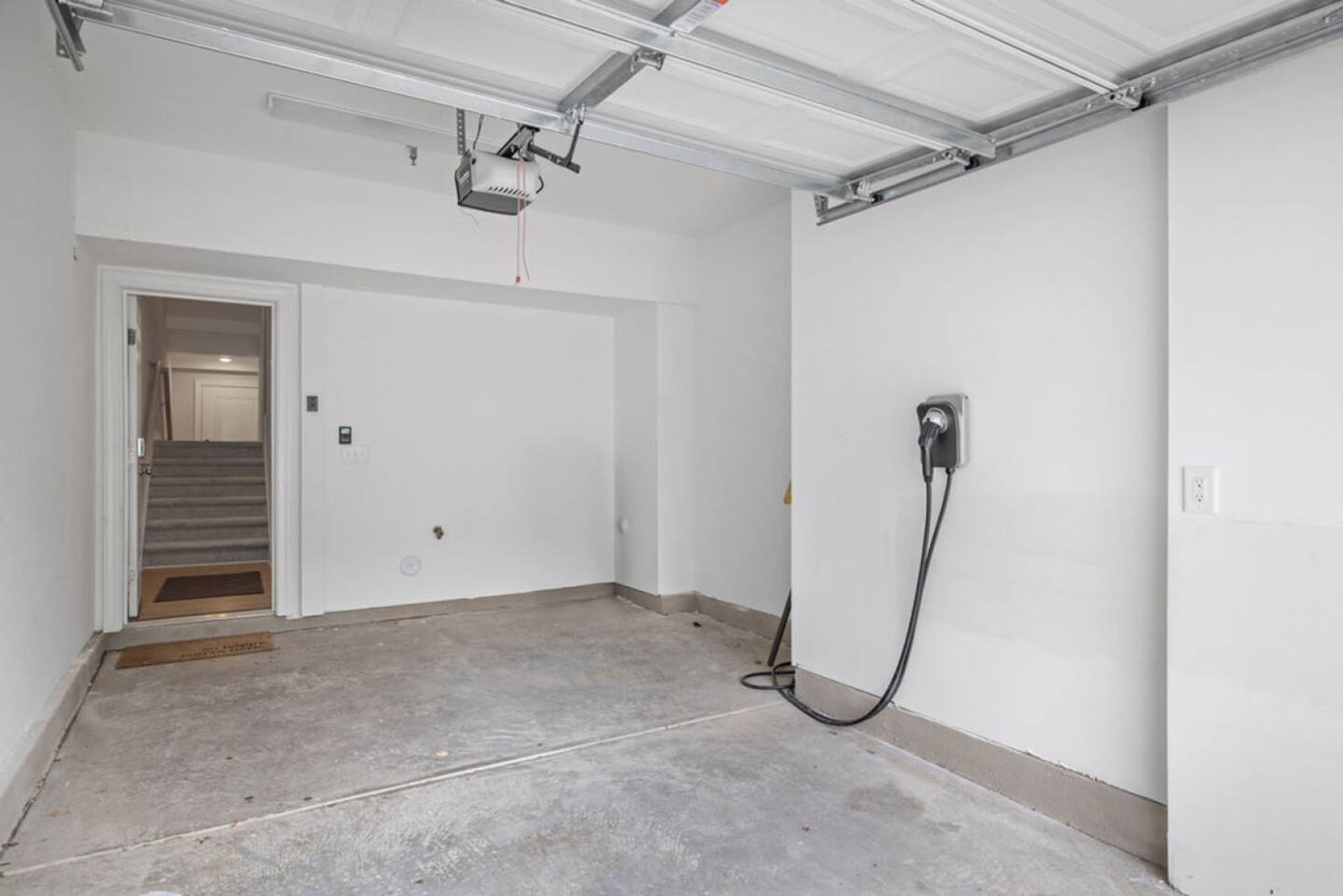 A clean, empty garage with a ceiling-mounted projector, a door leading to a stairwell, and a power outlet on the wall.
