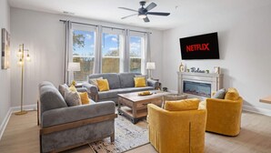 A modern living room with a grey sofa, yellow armchairs, a fireplace, and a Netflix sign on the wall. - NEW Luxury Condo Rooftop Terrace EV Charger (Wake Forest)