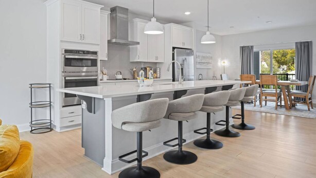 A modern kitchen with white cabinetry, a central island with bar stools, stainless steel appliances, and pendant lighting. - NEW Luxury Condo Rooftop Terrace EV Charger (Wake Forest)