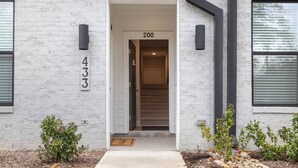 A building entrance with a white brick facade, a door labeled '200', and a small plant in the foreground. - NEW Luxury Condo Rooftop Terrace EV Charger (Wake Forest)