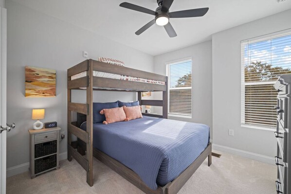 A bedroom with a bunk bed, a ceiling fan, a bedside table with a lamp, and a window with blinds. - NEW Luxury Condo Rooftop Terrace EV Charger (Wake Forest)