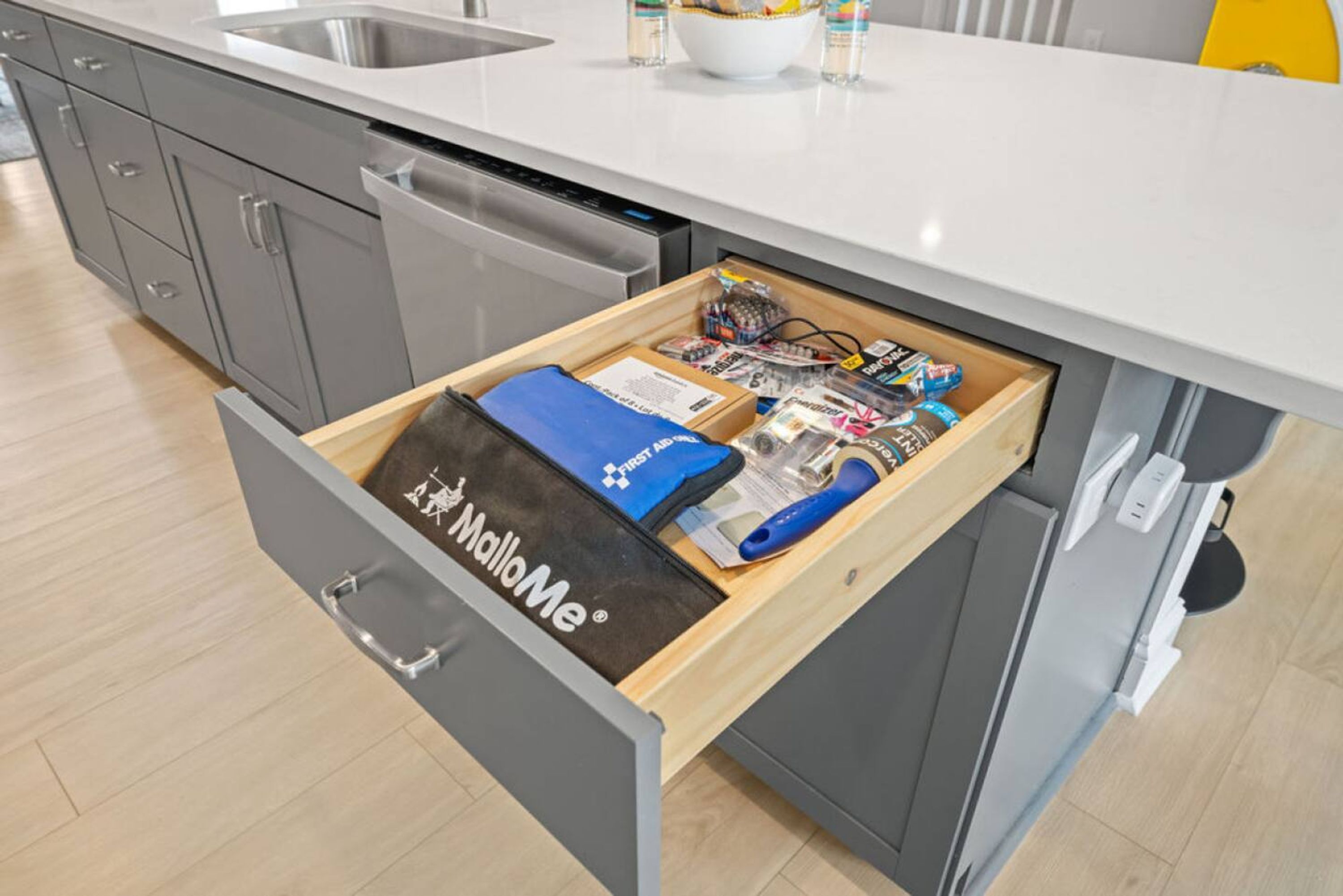 A kitchen with a drawer containing a blue bag, a white bowl, and various kitchen items.