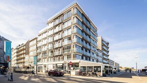 A multi-story hotel with a modern design, featuring balconies, a cafe, and a visible outdoor seating area. - 1 bedroom accommodation in Sint Idesbald (Sint Idesbald)