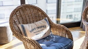 A wicker chair with a cushion labeled "SAINT-ROPEZ PROVENCE COTE D'AZUR" and a view of a building through a window. - 1 bedroom accommodation in Sint Idesbald (Sint Idesbald)