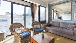 A living room with a sofa, two wicker chairs, a coffee table, and a large window with curtains. - 1 bedroom accommodation in Sint Idesbald (Sint Idesbald)