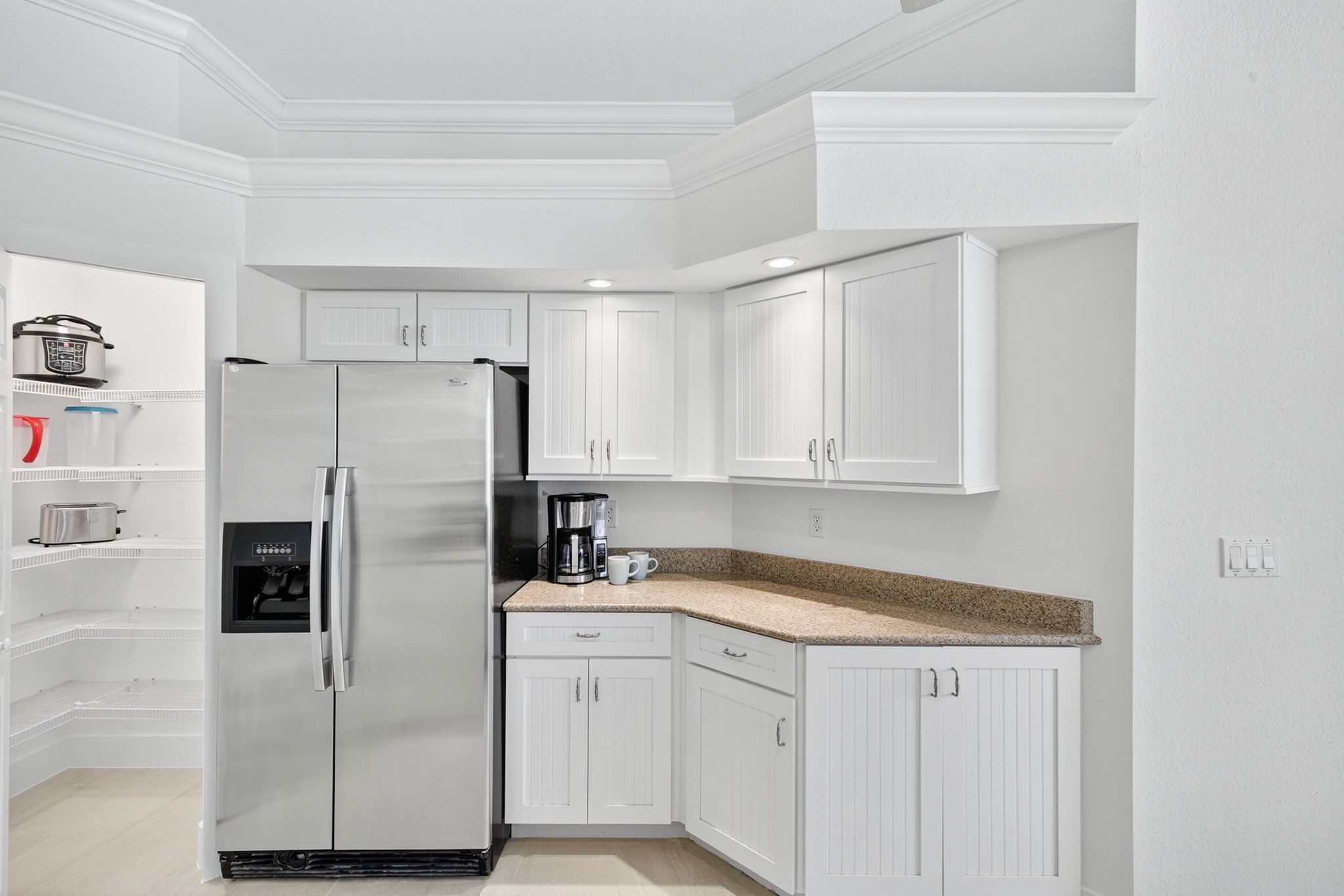 A modern kitchen with white cabinetry, a stainless steel refrigerator, a coffee maker, and a built-in oven.