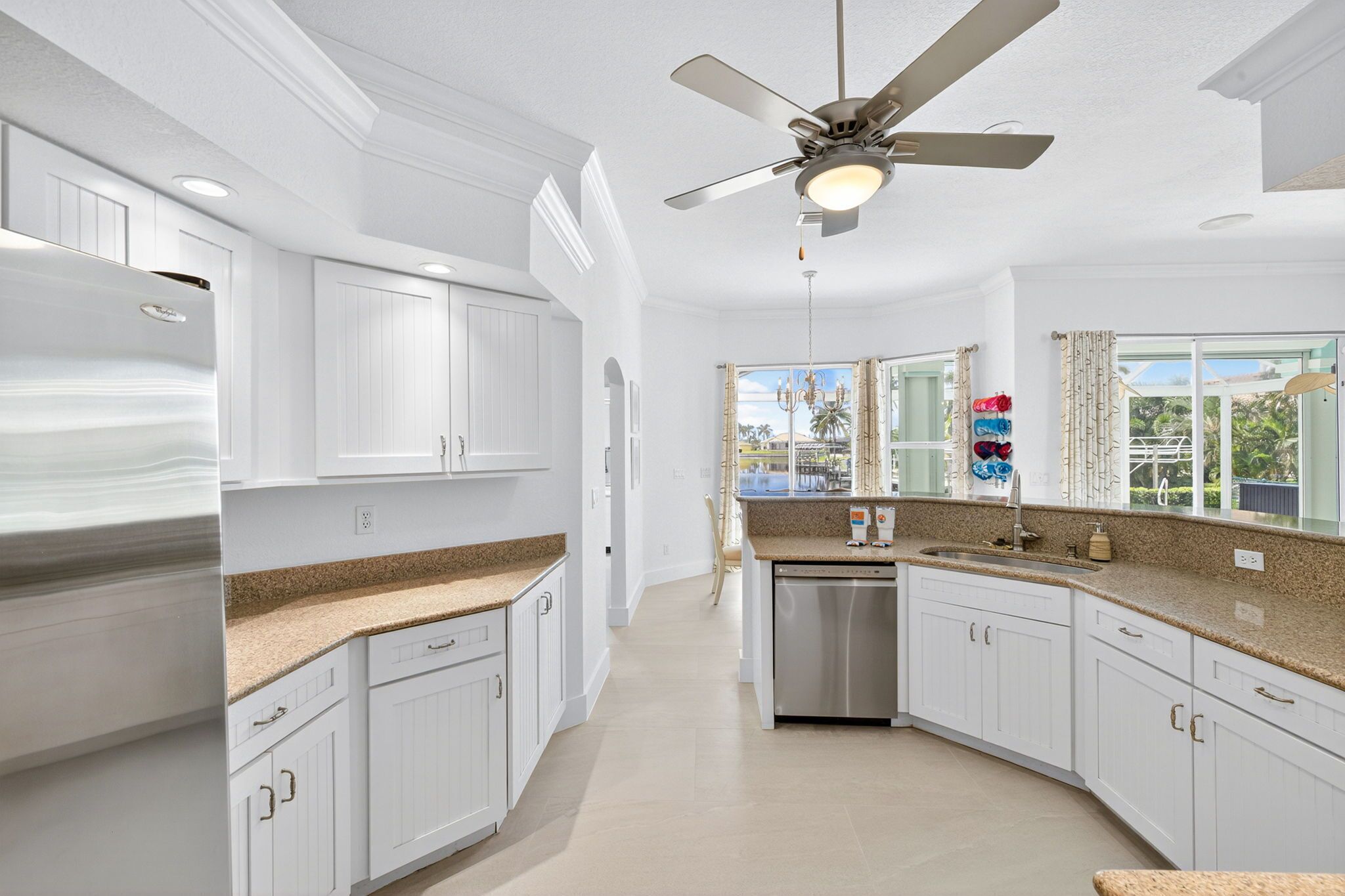 A modern kitchen with white cabinetry, granite countertops, a built-in dishwasher, and a ceiling fan.
