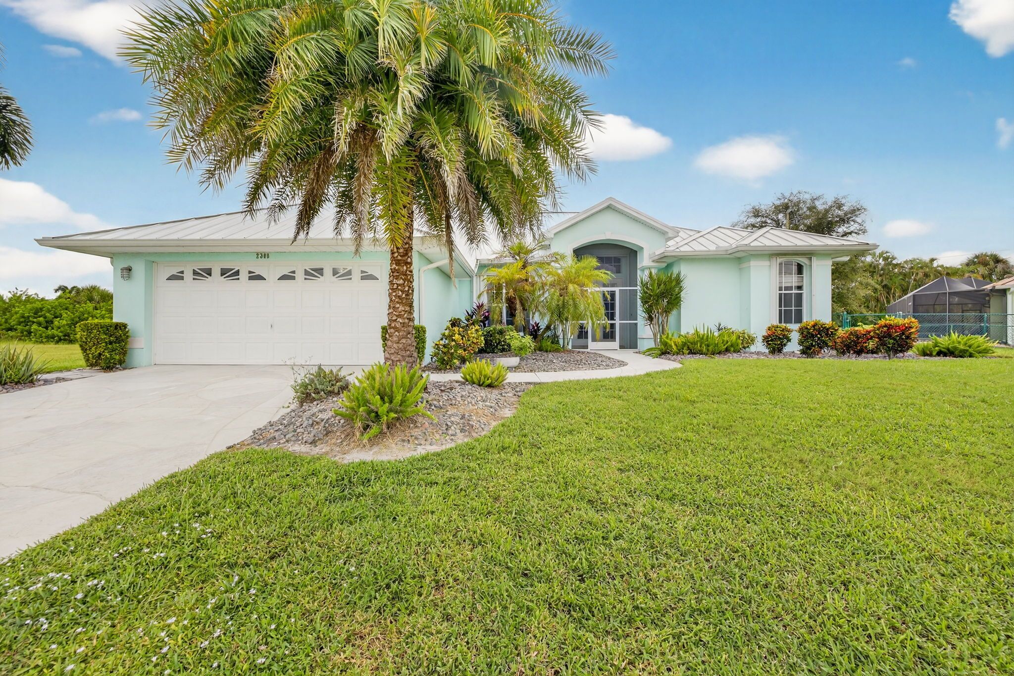 A light blue house with a garage, surrounded by a well-maintained lawn and various plants.