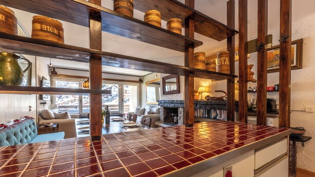 Una cocina con salpicadero de azulejos, vigas de madera y utensilios de cocina en estantes.
