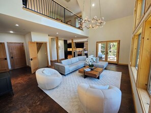 A spacious living area with a high ceiling, a built-in fireplace, a large sofa, a coffee table, and a view of the outdoors through a sliding glass door. - Cedar Rock Cabin: 5 bedroom in Mi-Wuk Village (Mi-Wuk Village)