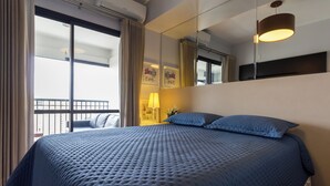 Et hotelværelse med en stor seng, et vindue med gardiner, et sengebord med lampe og et spejl på væggen.