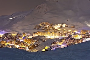 Un pueblo en la montaña cubierto de nieve en la noche, con edificios iluminados y una pista de esquí.