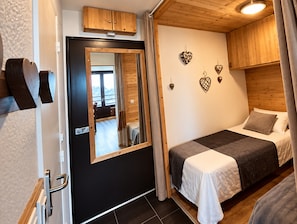 A bedroom with a bed, a mirror, wooden cabinets, and decorative heart-shaped items on the wall. - Apartment 'Higginson Val Thorens' with Mountain View and Balcony (Les Belleville)