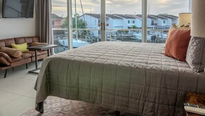 A bedroom with a large bed, a sofa, a small table, and a TV on the wall.