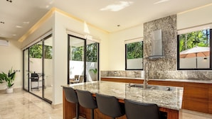 Una cocina moderna con encimera de granito, taburetes de bar y un ventanal con vistas a zonas verdes.