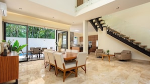 Un amplio salón con una mesa de comedor, asientos cómodos, una escalera y vistas al exterior.