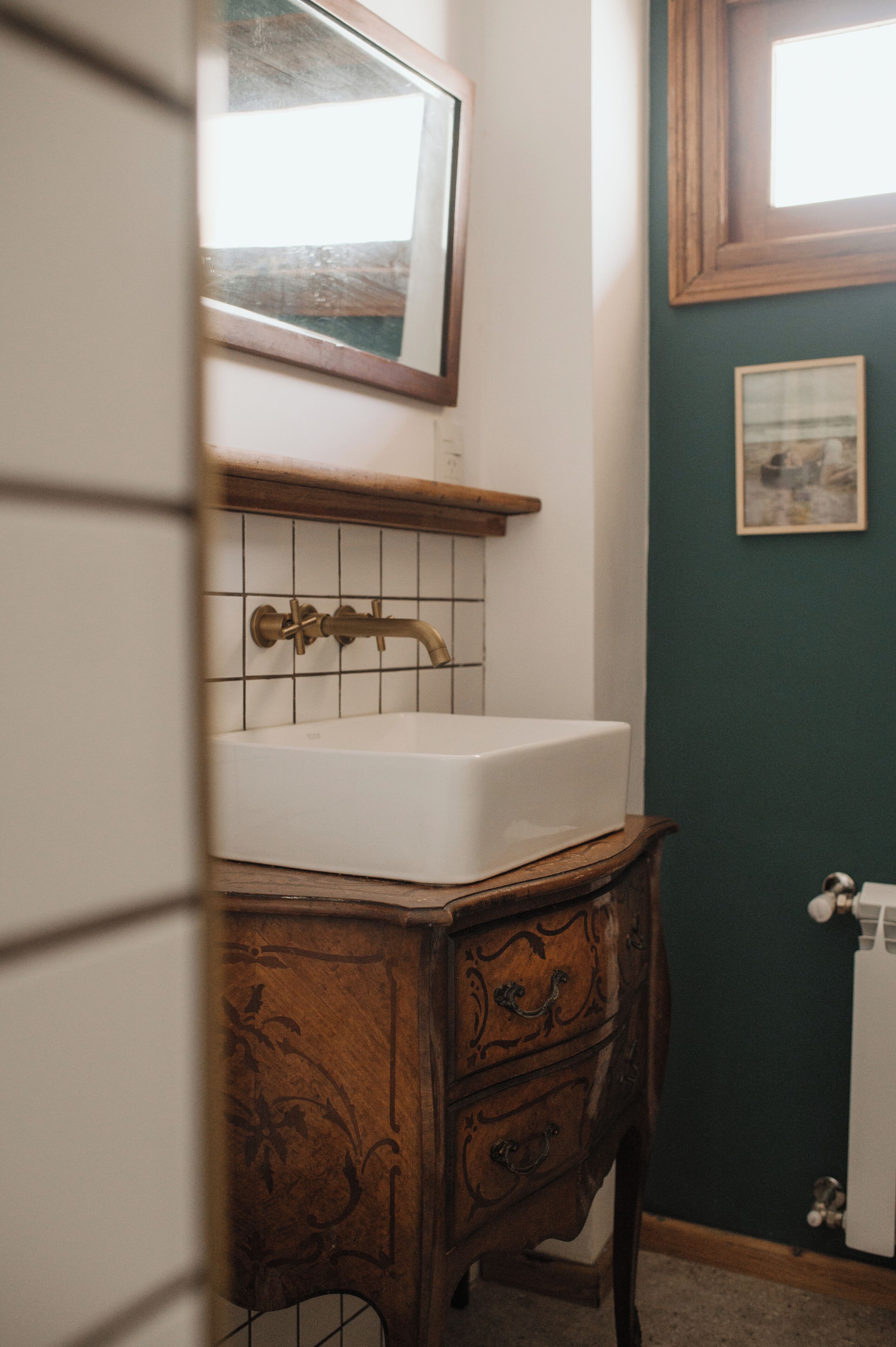 Un baño con lavamanos blanco, mueble de madera y espejo encima.