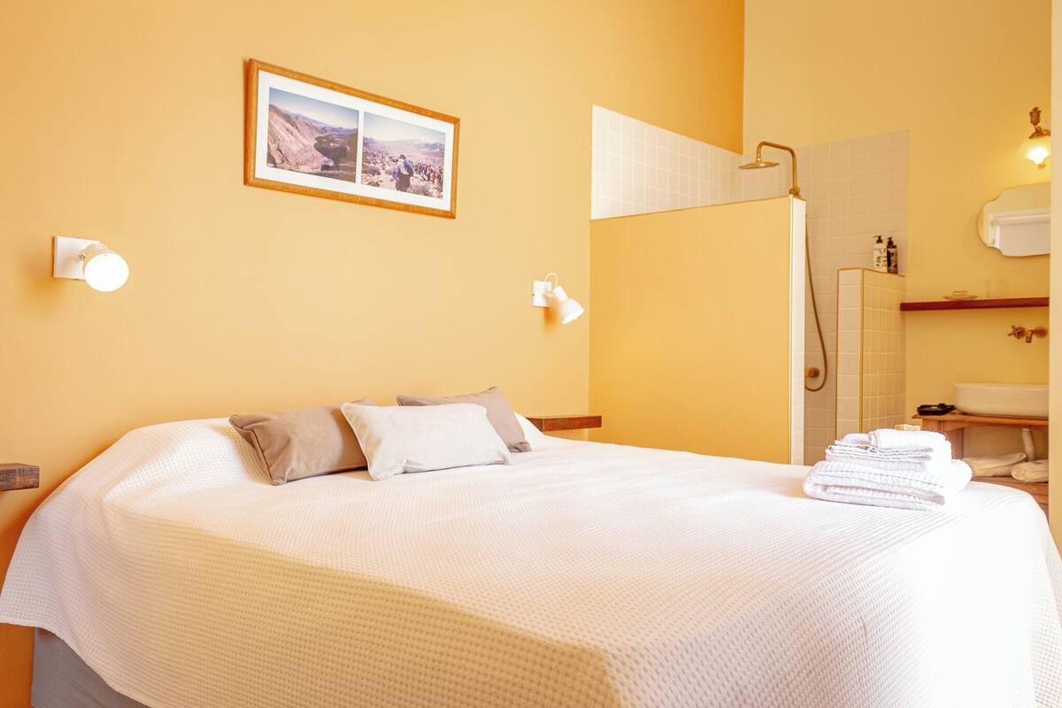 Een hotelkamer met een groot bed, een ingelijst kunstwerk aan de muur, en een badkamer met douche en wastafel.