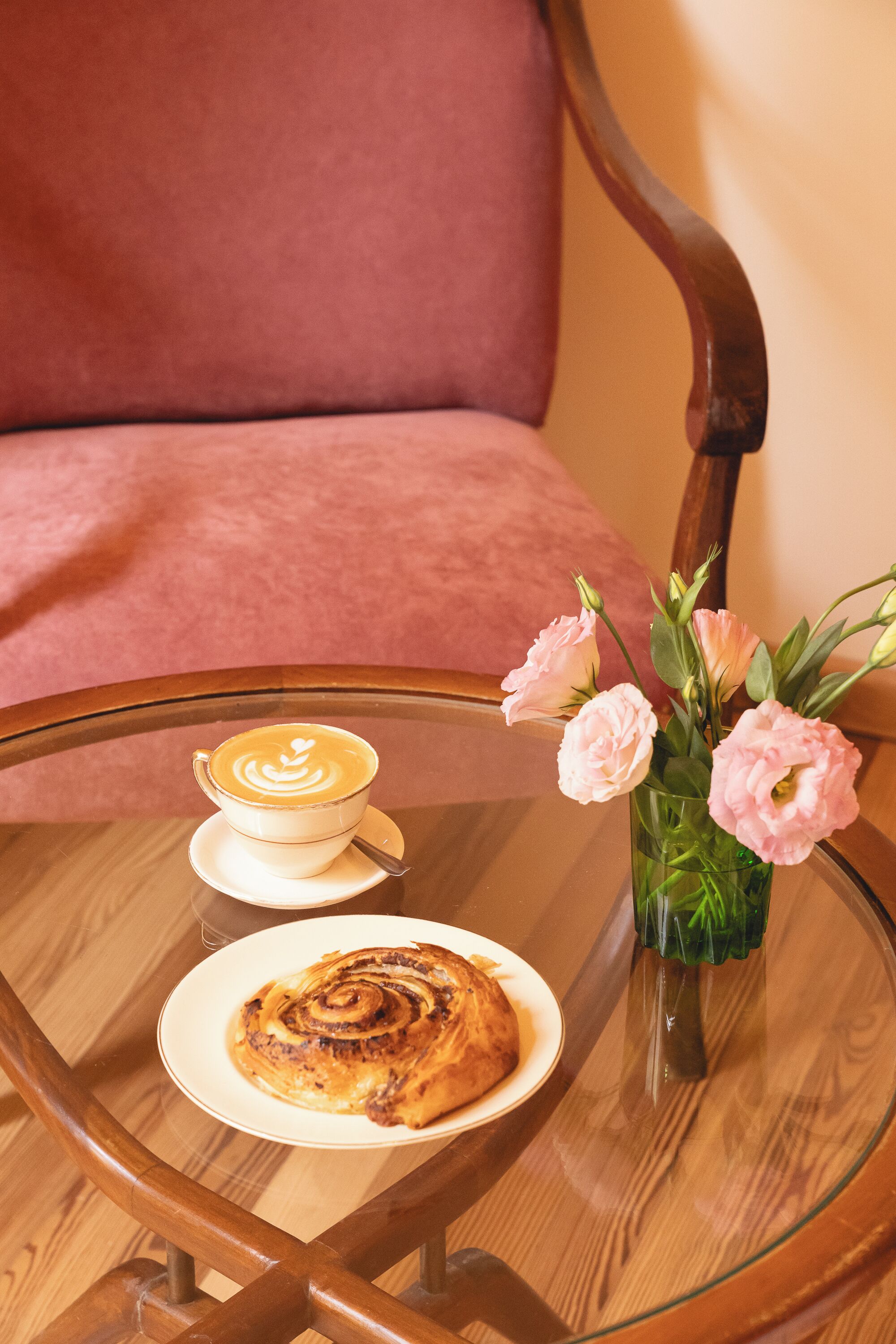 Ein Glastisch mit einem Teller Essen, einer Kaffeetasse und einer Vase mit Blumen.