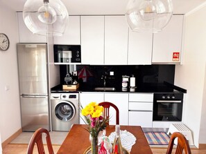 Cocina compacta con lavadora, horno y comedor con mesa y sillas.