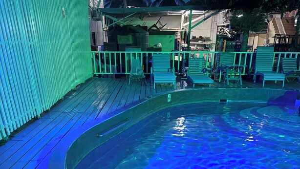 A circular hot tub with a wooden deck surrounding it, benches, and a green fence. - Chinatown hotel (Caye Caulker)
