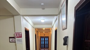 A hotel corridor with an exit sign, a fire alarm, and a door at the end. - Chinatown hotel (Caye Caulker)