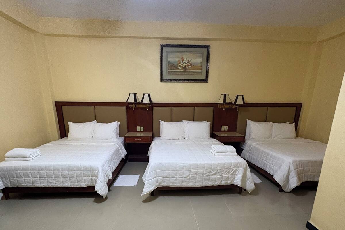 A hotel room with three single beds, a ceiling fan, and a framed picture on the wall.