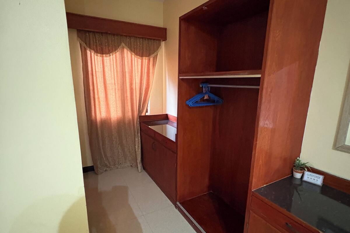 A room with a wooden wardrobe, a small table, and a window with curtains.