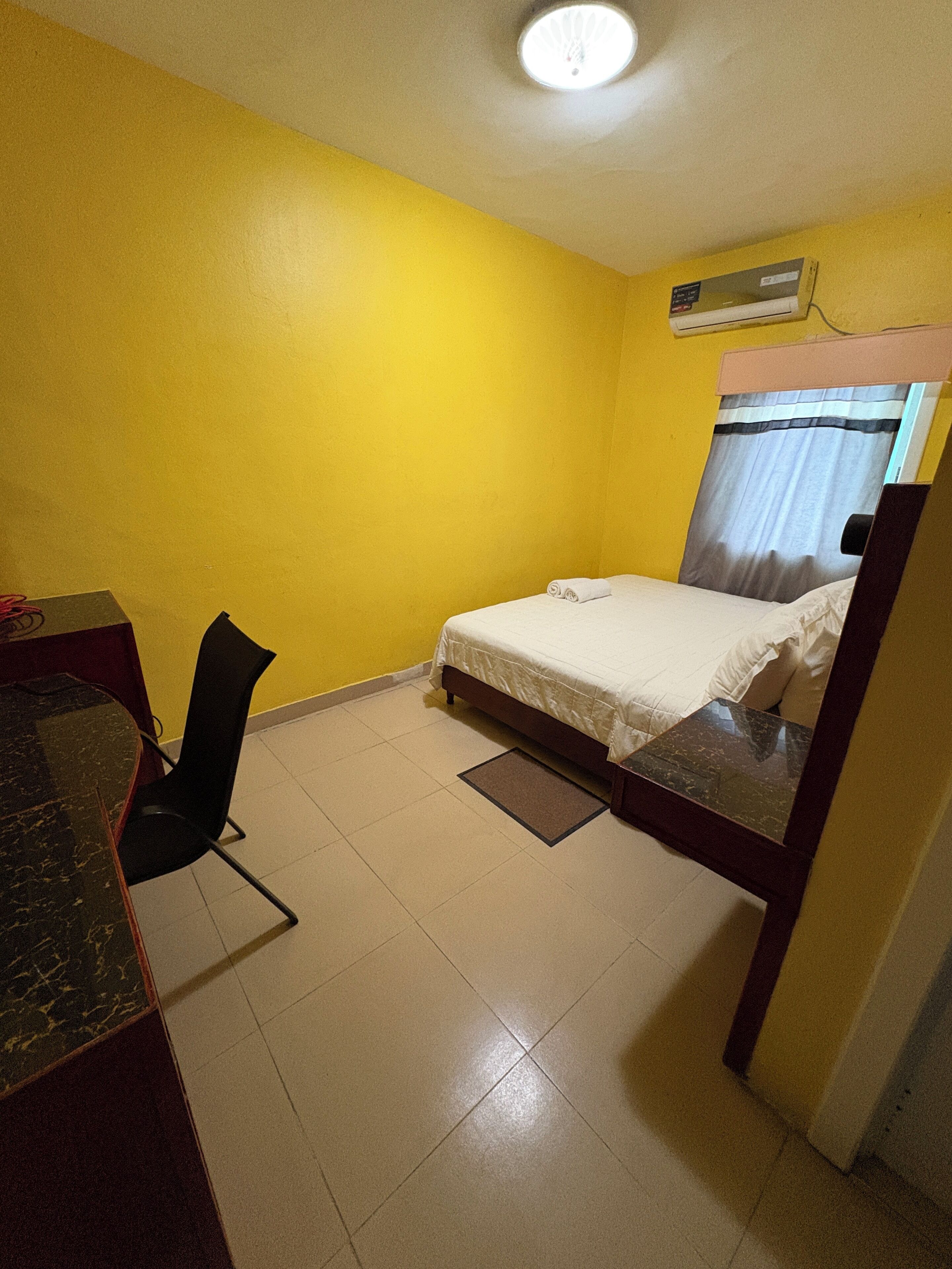 A small, yellow-walled room with a single bed, a chair, and a desk.
