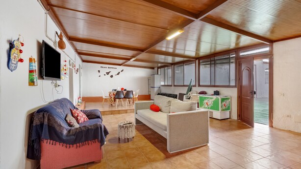 A living room with a sofa, a television, a small table, and a kitchen area with a refrigerator and a microwave. - Vacation Home 'La Casita Cueva Don Carmelo' with Mountain View, Private Terrace & Wi-Fi (San Bartolomé de Tirajana)