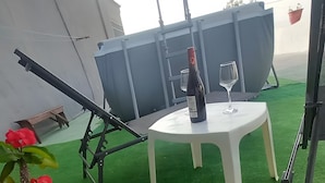 A rooftop terrace with artificial grass, a white table, a potted plant, and a wine bottle. - Vacation Home 'La Casita Cueva Don Carmelo' with Mountain View, Private Terrace & Wi-Fi (San Bartolomé de Tirajana)