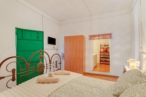 A bedroom with a bed, a green door, a wooden wardrobe, a television, and a view into another room.
