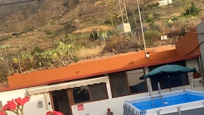 A swimming pool, a building with a red roof, and a mountainous backdrop. - Vacation Home 'La Casita Cueva Don Carmelo' with Mountain View, Private Terrace & Wi-Fi (San Bartolomé de Tirajana)