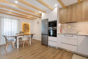 A modern kitchen with wooden beams, white cabinets, a stainless steel refrigerator, and a dining area with a table and chairs.