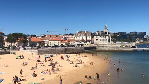A beach with people sunbathing and swimming, a historic building with a tower, and construction cranes in the background. - Zeca Holidays Atalaia Mezzanine Apartment with Balcony and Wi-Fi (Atalaia)