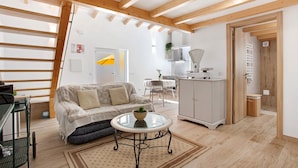A living room with a sofa, a glass coffee table, and a kitchen area with cabinets and a sink. - Zeca Holidays Atalaia Mezzanine Apartment with Balcony and Wi-Fi (Atalaia)