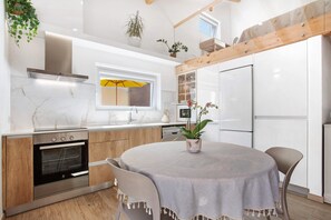 A modern kitchen with a built-in oven, a stove, and a refrigerator. There is a dining table with chairs and a potted plant on it.
