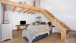 A bedroom with a wooden staircase, a bed with a patterned bedspread, a television, and a desk with a computer. - Zeca Holidays Atalaia Mezzanine Apartment with Balcony and Wi-Fi (Atalaia)